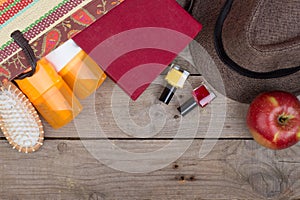Beach accessories hairbrush, orange towel, hat, sun cream, lotion, beach bag, nail polish, a book on a brown wooden background