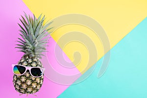 Beach accessories pineapple with pink sunglasses on pink, green and yellow background for summer holiday and vacation concept