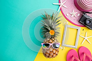 Beach accessories retro film camera, pineapple, sunglasses, flip flop starfish beach hat and sea shell on pink and yellow