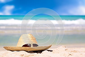 Beach accessories on sand for summer vacation concept. Straw hat with sunglasses on white sand against turquoise water amazing