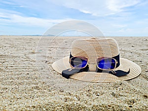 Beach accessories on the sand for summer vacation ideas, straw hat and sunglasses. White sand beach with ocean and blue sky as