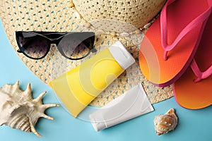 Beach accessories and sunscreen on light blue background, flat lay