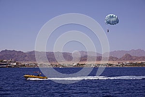 Beach activity: parasailing, high-speed boat pulls a man on a parachute. Sea and mountains on the background