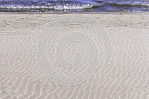 Beach background with smooth and textured lines in sand, breaking blue wave in distance
