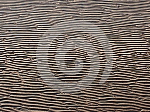 Beach background with wavy pattered surface formed by water on the wet sand and shadow