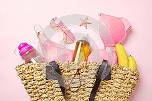 Beach bag with summer fashion clothing and accessories on pink background. Top view glamour feminine stuff, trendy swimwear,