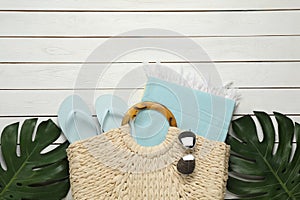 Beach bag with towel, flip flops and sunglasses on white wooden background, flat lay. Space for text