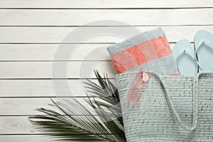 Beach bag with towel, flip flops and sunglasses on white wooden background, flat lay. Space for text