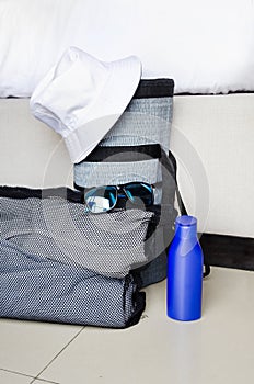 beach bag with towels, hat, rug, sun lotion, sunglasses are on floor in hotel room