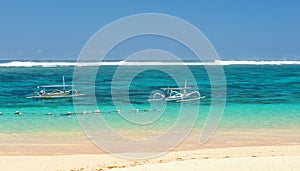 Beach in Bali with sea views and two small boats with the coast line on a Sunny day with small clouds on the horizon the