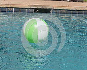 Beach ball in blue swimming pool near depth sign on edge