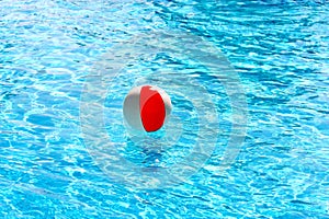 Beach ball floating in a pool with small waves reflecting in summer sun