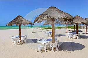 Beach bar - Tiki thatch umbrellas on sandy beach with white plastic chairs underneath and the turquioise sea and very blue sky on