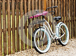 Beach bike parked against a fence with umbrellas in its basket