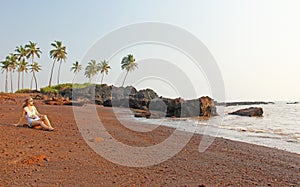 Beach with black sand and palm trees. Dark brown volcanic sand a