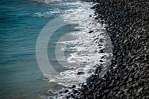 Beach of black volcanic rocks at the shore line.