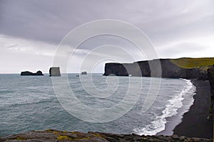 Beach with black volcanic sand and a rock in the middle of the sea Iceland northen Europe during a very cloudy and dark day