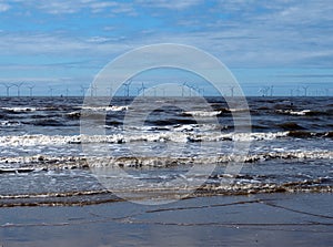 Beach at blundell flats in southport with waves braking on the beach and the wind turbines at burbo bank visible in the