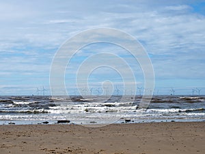 the beach at blundell sands in southport with waves braking on the beach and the wind turbines at burbo bank visible in the