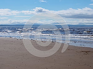 The beach at blundell sands in southport with waves braking on the beach and the wind turbines at burbo bank visible in the