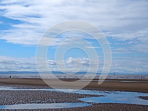 Beach at blundell sands in southport with waves breaking on the beach and the mersey coastline in the distance and a flock of