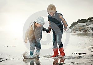 Beach, boots and children in water together, holding hands and playing in waves with smile. Fun, holiday and brothers