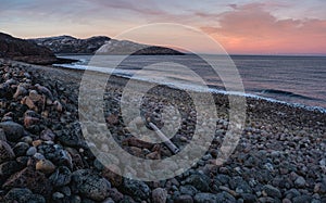 Beach with boulders. A log washed ashore by a storm. Wonderful panoramic mountain landscape on the Barents sea. Teriberka