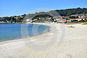 Beach with bright sand and turquoise water. Coastal village, trees and blue sky. Galicia, Spain.