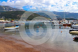 Beach and pier in Budva, Montenegro, Balkans, Adriatic Sea. Yachts and boats in the bay. Mountains and clouds.