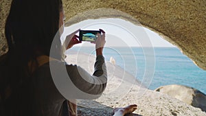 Beach, cave and woman with phone for picture, photography and memories of holiday, vacation and scenic view. Travel