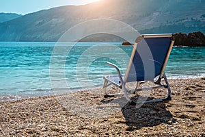 Beach chair from back on tranquil pebble beach. Amazing view to impressive rocks in the water. Serenity and isolation on