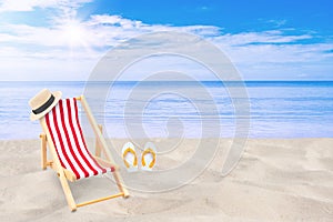 Beach chair, weave hat and white sandal flip flop on sand beach with beautiful seascape view of sea and blue sky in the background