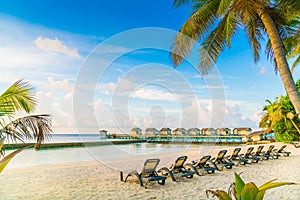 Beach chairs in Maldives island with water villas at the sunrise