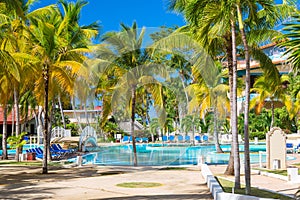 Beach chairs near swimming pool in tropical resort with palm trees