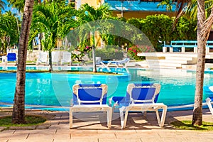 Beach chairs near swimming pool in tropical resort with palm trees