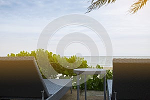 Beach chairs with table on the beach under the palm tree in front of the sea. Look ahead to the sea. Can be use as background of a