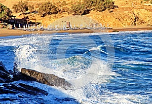 Beach chairs and waving sea at resort in village panormos at Crete island in Greece