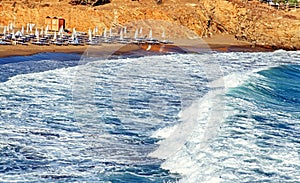 Beach chairs and waving sea at resort in village panormos at Crete island in Greece