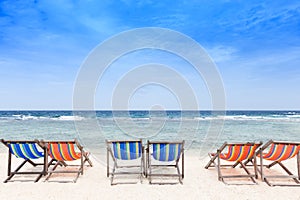 Beach chairs on the white sand beach with cloudy blue sky.
