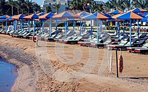 Beach with chaise lounges standing in line on beige sand. Holiday and travel concept