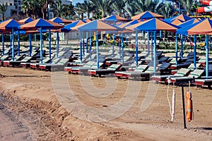 Beach with chaise lounges standing in line on beige sand. Holiday and travel concept