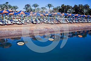 Beach with chaise lounges standing in line on beige sand. Holiday and travel concept