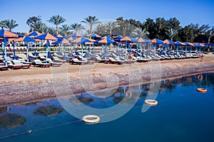 Beach with chaise lounges standing in line on beige sand. Holiday and travel concept