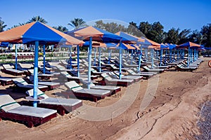 Beach with chaise lounges standing in line on beige sand. Holiday and travel concept