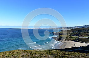 Beach with cliff and port. Blue sea with waves and white foam. Sunny day, Arteijo, Coruna, Spain.