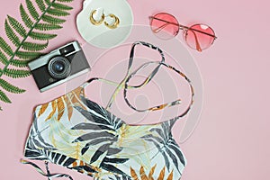 Beach concept with camera, sunglasses, green leave and hat over the pink background.