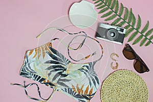 Beach concept with camera, sunglasses, green leave and hat over the pink background.