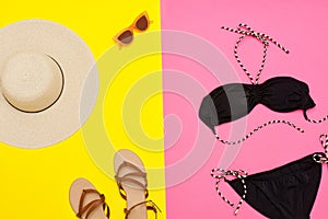 Beach concept. Women`s hat, sandals, black swimsuit, glasses. Yellow with pink background, top view