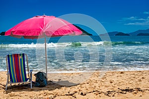 Beach day. Colorful beach chair under a pink umbrella on the beach sand on a sunny day with a blue sky