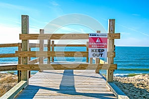 Beach erosion warning sign on wooden barrier